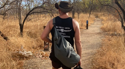 A man walking in dry bushland wearing a North Storm 20L Dry Bag. 