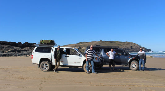 FOUR MATES STANDING BY THEIR FOUR WHEEL DRIVES ON A CLEAR DAY ON A BEACH IN COFFS HARBOUR,