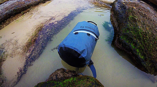 A North Storm® Waterproof Dry Bag floating in some water on a beach. 