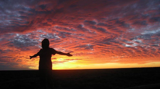 A silhouette of a lady standing with her arms outstretched with a beautiful sunset behind her. 