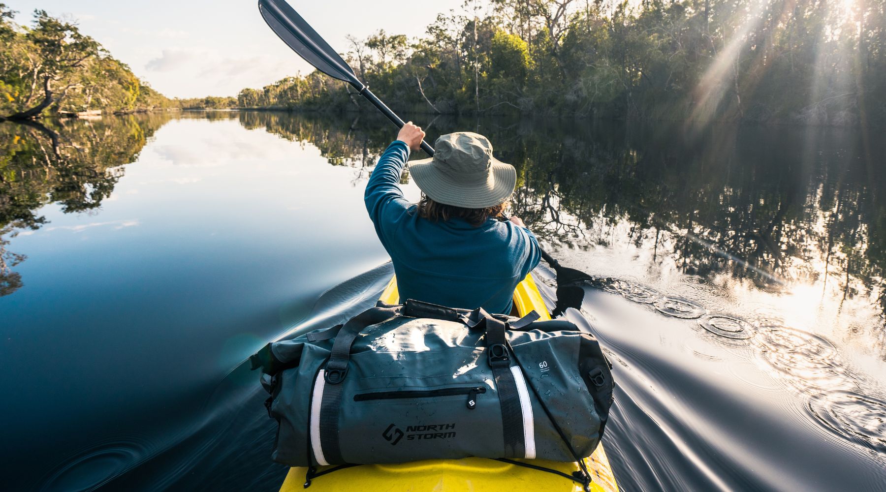 Man_paddling_a_kayak_on_the_river with his 60L Waterproof North Storm duffel bag on the back.