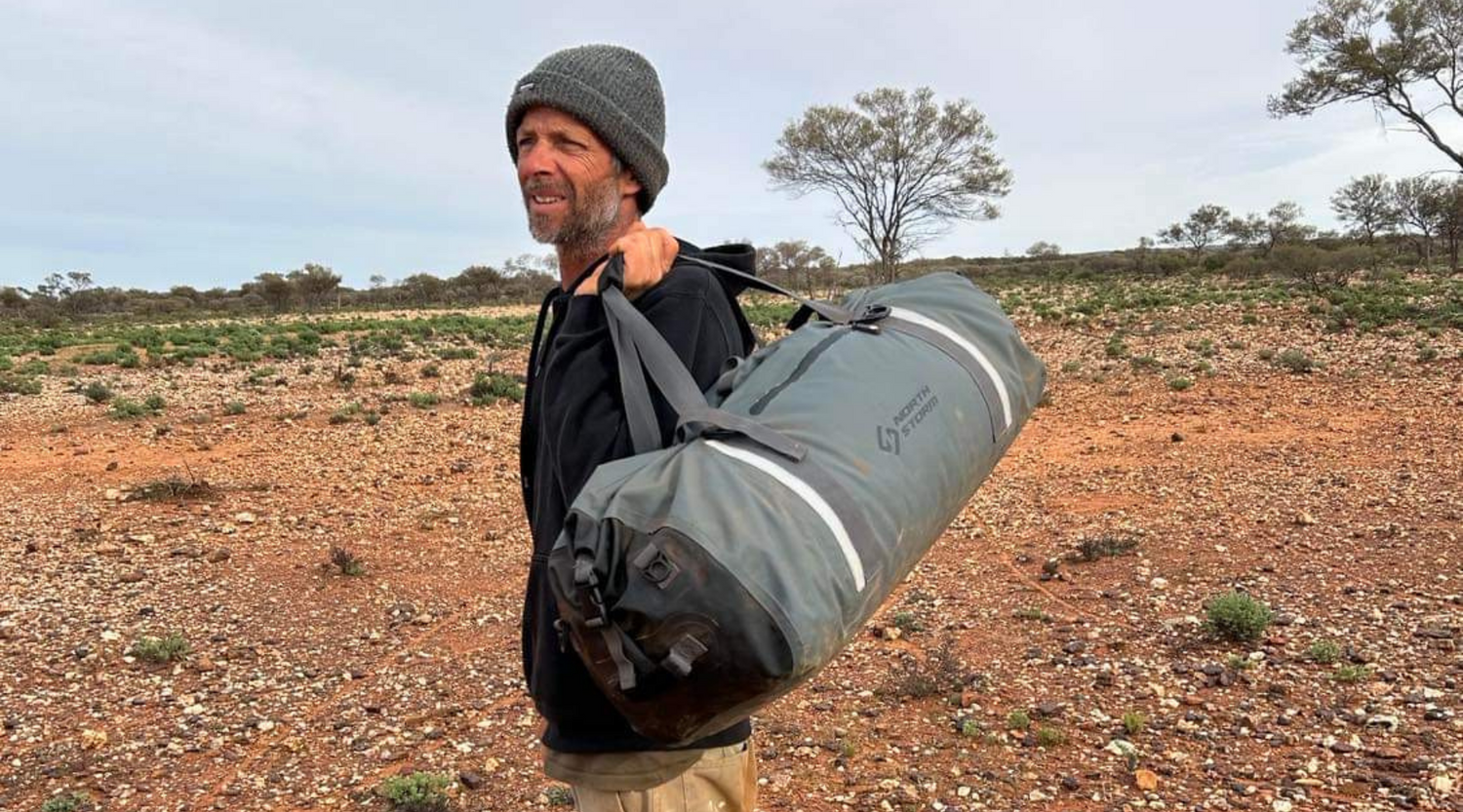 Man holding a North Storm waterproof duffel bag standing in the outback of Western Australia.