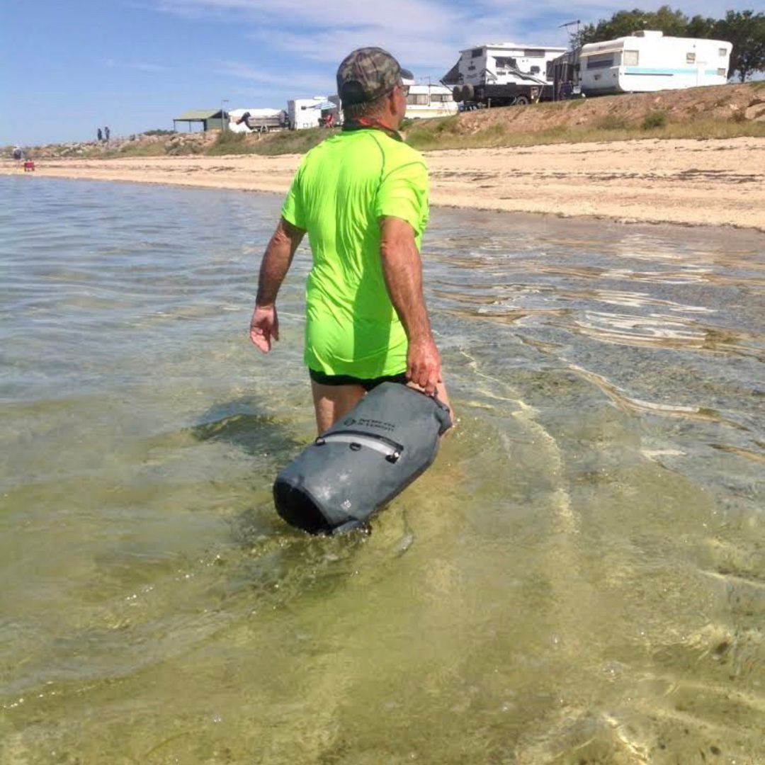 MAN DRAGGING A NORTH STORM WATERPROOF DRY BAG THROUGH THE WATER AT BLACKPOINT IN SOUTH AUSTRALIA - AUSTRALIA.