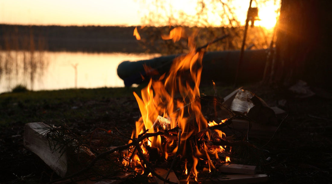 A CAMPFIRE BY A RIVER AT SUNSET.